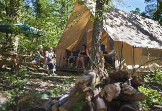 Family camping in front of a Canadienne safari tent at Village Huttopia Lanmary, France, surrounded by trees.
