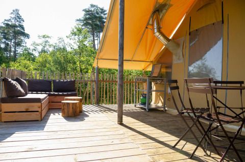 Terraza de madera con zona de estar, mesa y sillas bajo una tienda safari en Village Huttopia Lanmary, Francia.