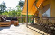 Terraza de madera con zona de estar, mesa y sillas bajo una tienda safari en Village Huttopia Lanmary, Francia.