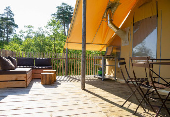 Terrazza in legno con area salotto, tavolo e sedie sotto tenda safari al Village Huttopia Lanmary, Francia.
