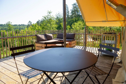 Terrazza esterna con tavolo rotondo nero, sedie e divano in una tenda Trappeur al Village Huttopia Lanmary, Francia.