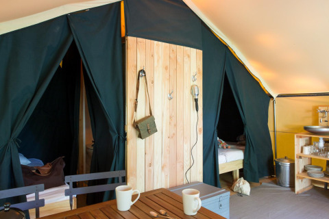 Indretningen af et safari Trappeur-telt på Village Huttopia Lanmary i Frankrig med senge og køkkenområde.