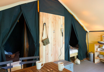 Indretningen af et safari Trappeur-telt på Village Huttopia Lanmary i Frankrig med senge og køkkenområde.