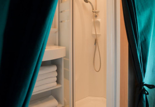 Badkamer met douche, handdoeken op planken en groene gordijnen in Trappeur-tent bij Huttopia Lanmary.