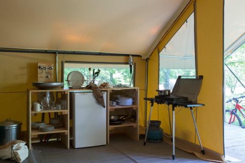 Cocina dentro de la tienda safari Trappeur I en Village Huttopia Lanmary, Francia, con estufa y refrigerador.