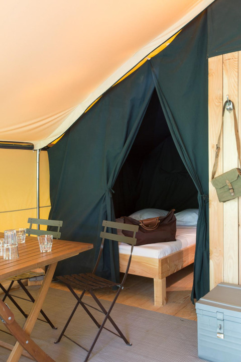 Binnenzicht van Trappeur tent I bij Village Huttopia Lanmary in Frankrijk met bed, tafel en stoelen.