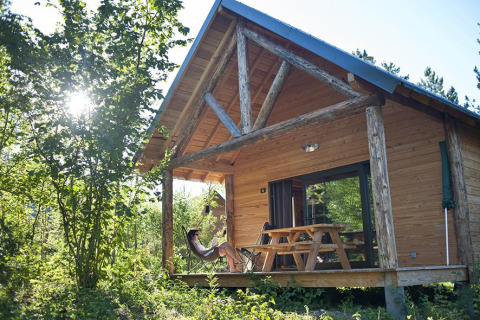 Kvinde slapper af udenfor en træhytte med veranda ved Village Huttopia Lanmary, omringet af natur.