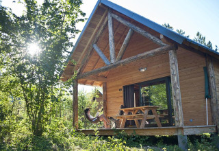 Mujer relajándose frente a una cabaña de madera en Village Huttopia Lanmary, Francia, rodeada de naturaleza.