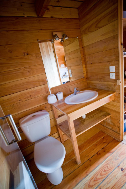 Baño compacto con inodoro moderno y lavabo, rodeado de paneles de madera cálida en una cabaña.