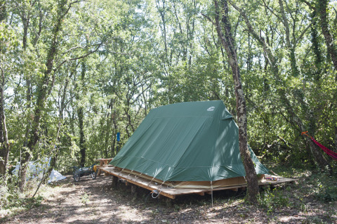 Grünes Bonaventure-Tipizelt auf Holzplattform im Wald bei Village Huttopia Sud-Ardèche, Frankreich.