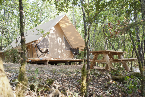 Tenda safari Canadienne con terrazza in legno e tavolo da picnic nel bosco al Village Huttopia Sud-Ardèche, Francia.