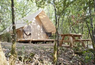 Tienda safari Canadienne con terraza de madera y mesa de picnic en el bosque de Village Huttopia Sud-Ardèche, Francia.