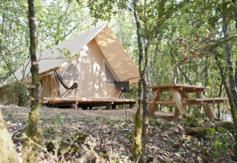 Safari-Zelt Canadienne mit Holzterrasse und Picknicktisch im Wald bei Village Huttopia Sud-Ardèche, Frankreich.