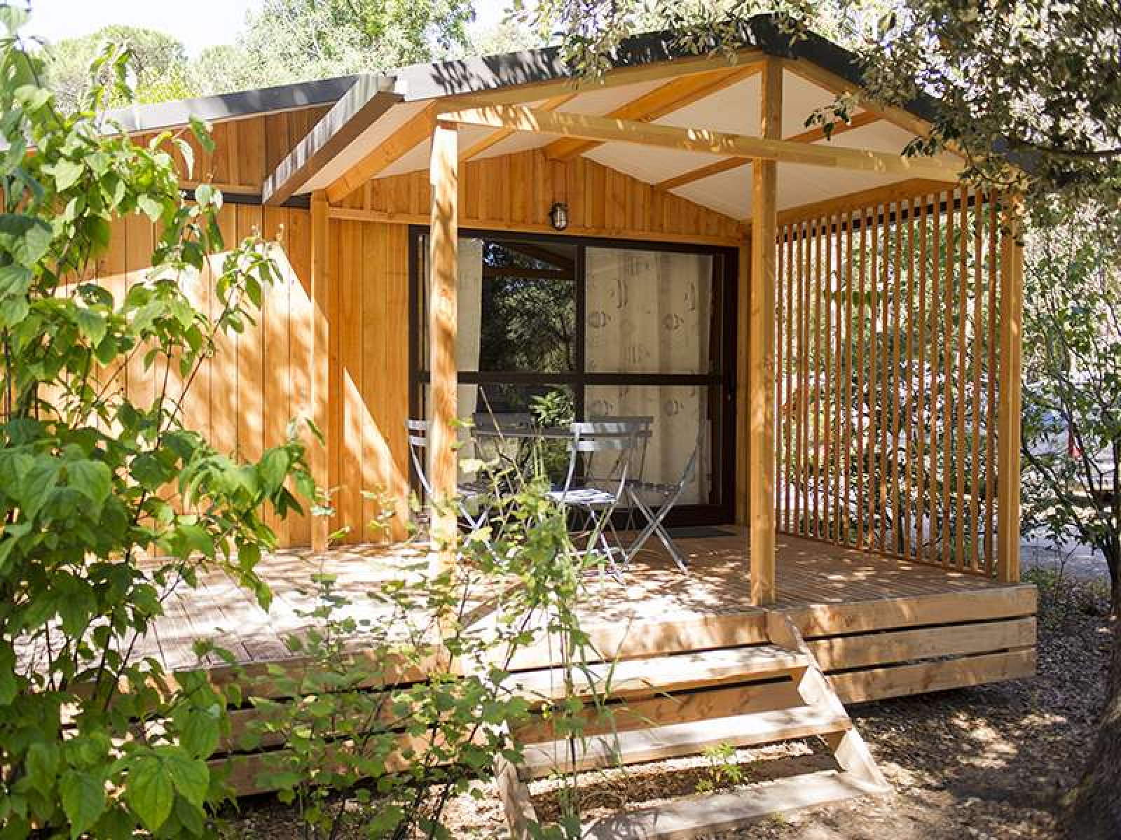 Een houten chalet met overdekt terras en buitenstoelen, omgeven door groen, bij Chalet Evasion in Frankrijk.