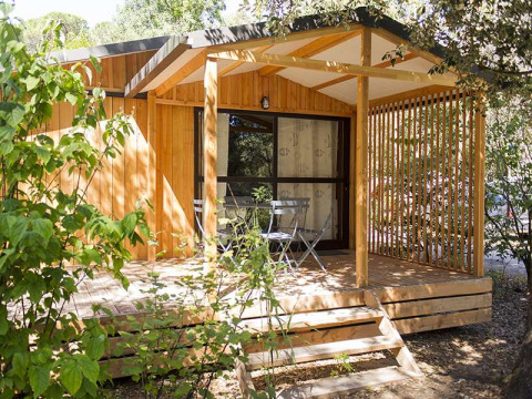 En træhytte med en lille terrasse og havemøbler, omgivet af grønne planter, ved Chalet Evasion i Frankrig.