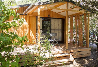 Eine Holzhütte mit Terrasse und Gartenmöbeln, umgeben von Bäumen, bei Chalet Evasion in Frankreich.