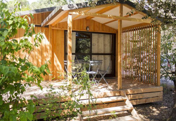 Chalet en bois avec terrasse couverte et chaises de jardin, entouré de verdure, à Chalet Evasion en France.