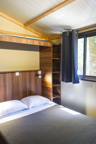 Vista interior de Chalet Evasion en Huttopia La Forêt de Janas, Francia, con cama, ventana y estanterías.