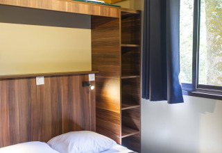 Vista interior de Chalet Evasion en Huttopia La Forêt de Janas, Francia, con cama, ventana y estanterías.