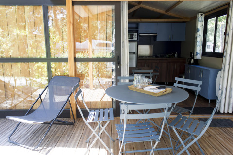 Udendørs terrasse med blå stole, bord og liggestol ved Chalet Evasion, Huttopia La Forêt de Janas, Frankrig.