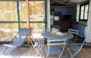 Udendørs terrasse med blå stole, bord og liggestol ved Chalet Evasion, Huttopia La Forêt de Janas, Frankrig.