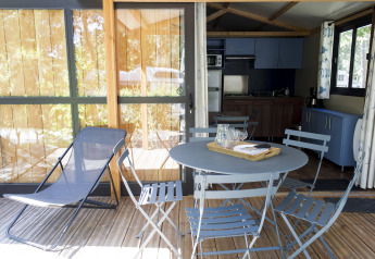 Udendørs terrasse med blå stole, bord og liggestol ved Chalet Evasion, Huttopia La Forêt de Janas, Frankrig.