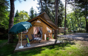 Tienda safari Trappeur en Huttopia La Forêt de Janas, Francia, rodeada de bosque, bicicleta y terraza cómoda.