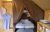Interior de una tienda Trappeur en Huttopia La Forêt de Janas, Francia, con cama y zona de lavabo visible.