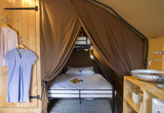 Interior de una tienda Trappeur en Huttopia La Forêt de Janas, Francia, con cama y zona de lavabo visible.