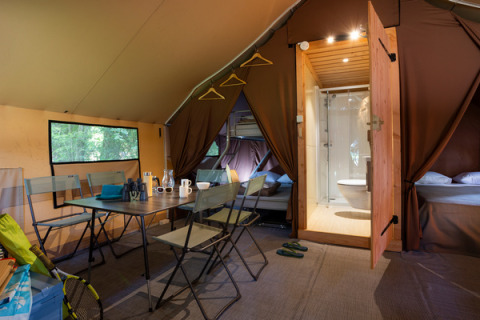 Binnenzicht van een Trappeur safaritent met eettafel, bedden en badkamer bij Huttopia La Forêt de Janas.
