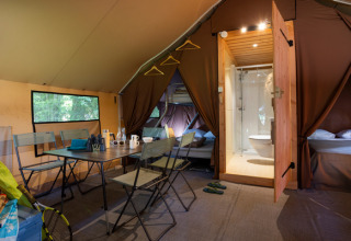 Vista interna di una tenda safari Trappeur con tavolo da pranzo, letti e bagno a Huttopia La Forêt de Janas, Francia.