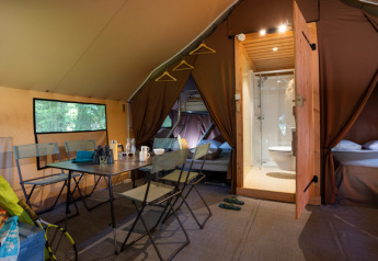Interior view of a Trappeur safari tent with dining table, beds, and bathroom at Huttopia La Forêt de Janas, France.