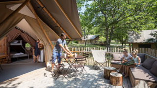Familia disfruta al aire libre en la terraza de una tienda safari Trappeur, rodeada de muebles y naturaleza.