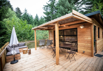 Udendørs træterrasse ved Chalet Toronto med siddepladser og parasol omgivet af frodig skovnatur.