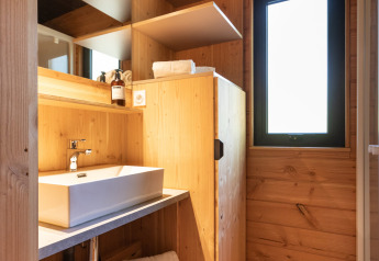 Moderne badkamer met houten wanden, wastafel, spiegel, open planken en raam bij Chalet Toronto, Village Huttopia.