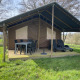 Udendørs lodge med overdækket terrasse, bord og stole samt liggestole på Camping La Colline i Belgien.
