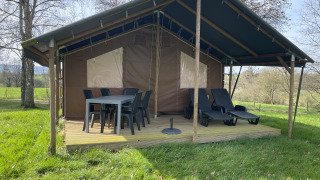 Outdoor-Lodge mit überdachter Terrasse, Esstisch, Stühlen und Liegen auf Camping La Colline in Belgien.