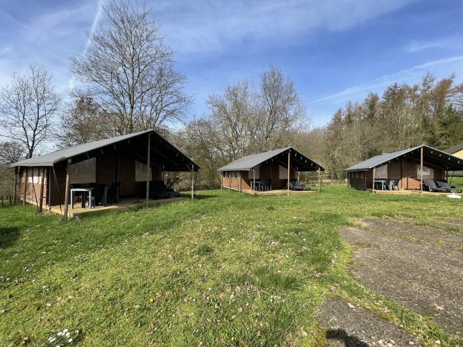 Drie Coco-lodges bij Camping La Colline in België, op een grasveld met bomen en een heldere blauwe lucht.