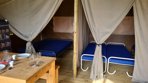 Innenansicht der Coco-Lodge auf Camping La Colline in Belgien mit Betten und Esstisch.