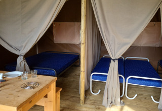 Innenansicht der Coco-Lodge auf Camping La Colline in Belgien mit Betten und Esstisch.