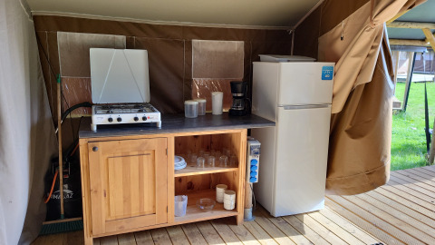 Küchenbereich einer Coco-Lodge auf Camping La Colline in Belgien mit Herd, Kühlschrank und Schrank.