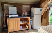 Kitchen area in a Coco lodge at Camping La Colline in Belgium with stove, fridge, and wooden cabinet.