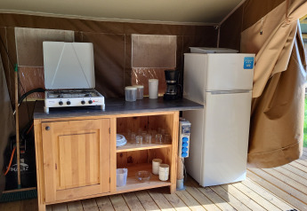 Zona de cocina en una lodge Coco en Camping La Colline, Bélgica, con estufa, frigorífico y armario.