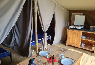 Intérieur d’un lodge Coco au Camping La Colline en Belgique, avec lits, table à manger et kitchenette.