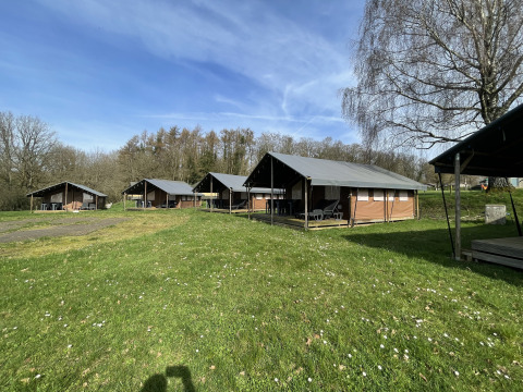 Mehrere Lodges auf einer Wiese beim Camping La Colline, Coco Lodge, Belgien, unter blauem Himmel.