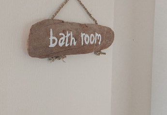 Ein Holzschild mit der Aufschrift 'bath room' hängt an einer weißen Tür im Beach House am Beloofde Land, Niederlande.