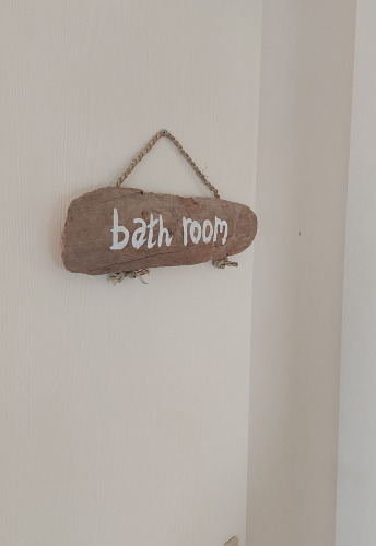 Un'insegna di legno con la scritta 'bath room' appesa a una porta bianca al Beach House, Beloofde Land, Paesi Bassi.