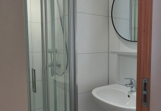 Baño moderno con cabina de ducha, lavabo y espejo redondo en Beach House en Beloofde Land, Países Bajos.