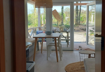 Interior de casa de playa luminosa con mesa de comedor, sillas y terraza con vistas a la naturaleza en Beloofde Land.