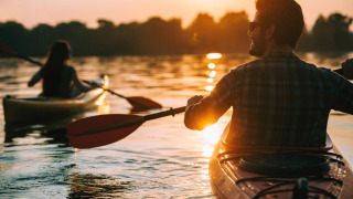 Dos personas en kayak remando al atardecer en un lago de un parque vacacional con alojamiento glamping.